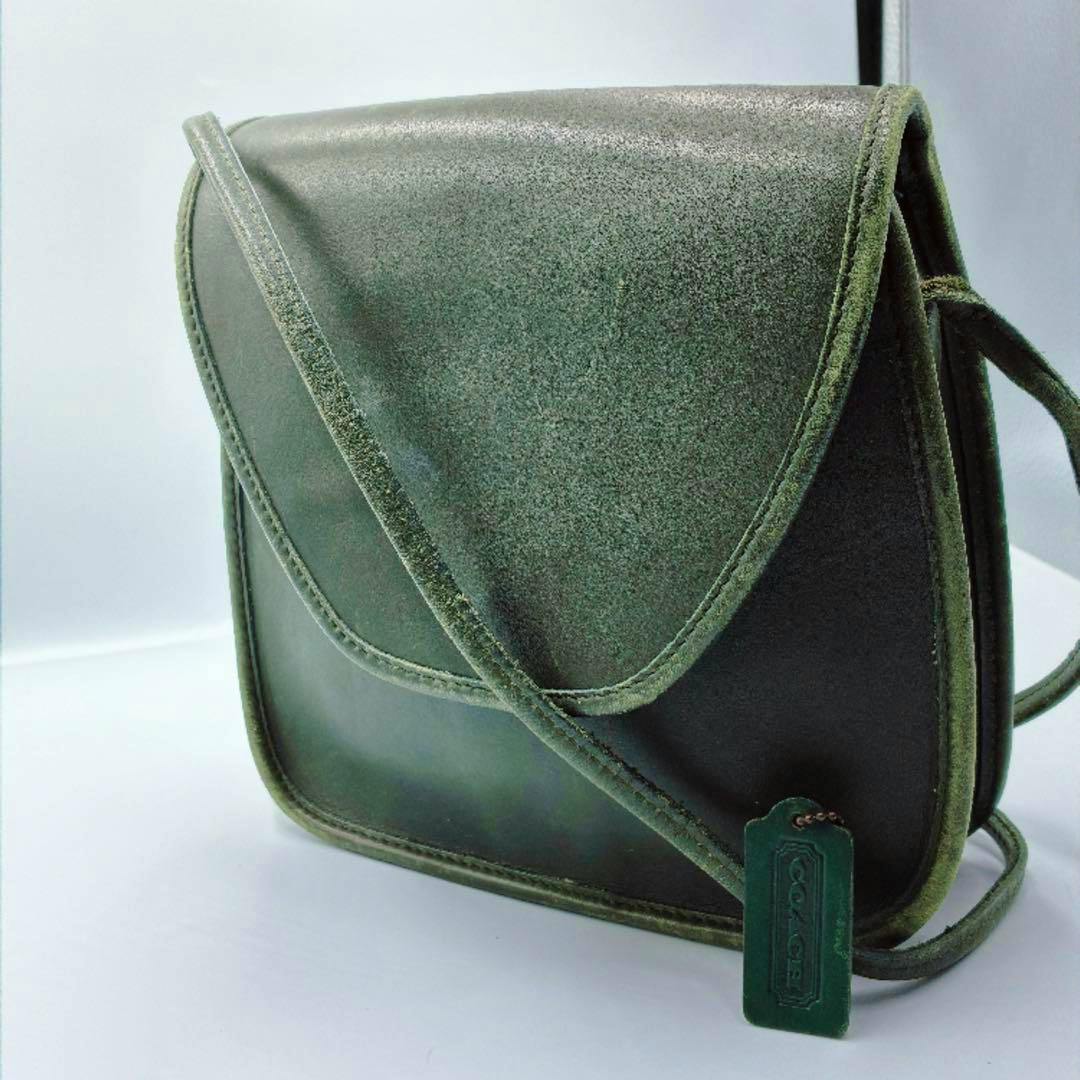 Green leather Coach shoulder bag with a flap closure and a hanging Coach tag on a white background.