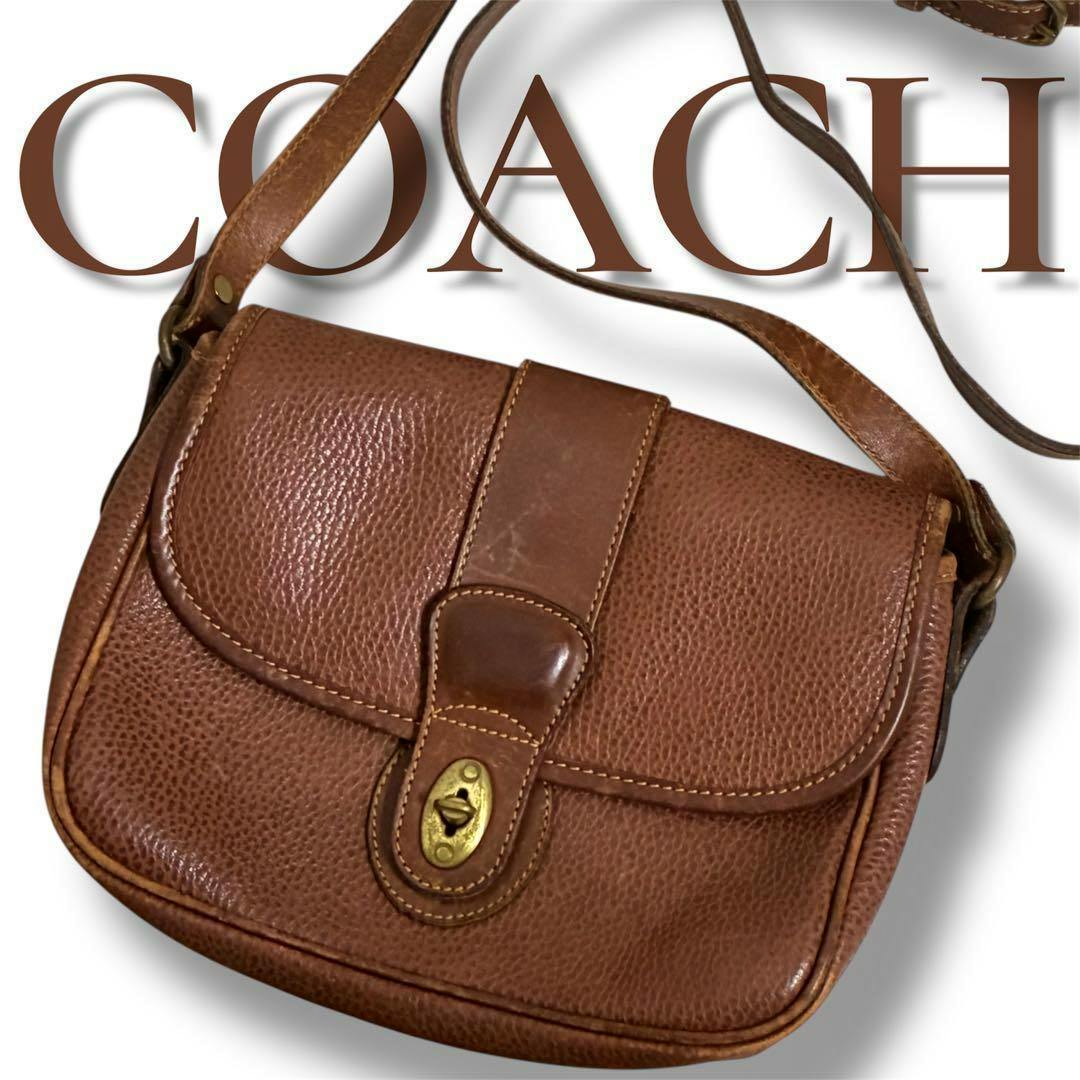 Brown cow-leather Coach shoulder bag with a front turnlock closure and adjustable strap, shown against a white background with a COACH logo behind.