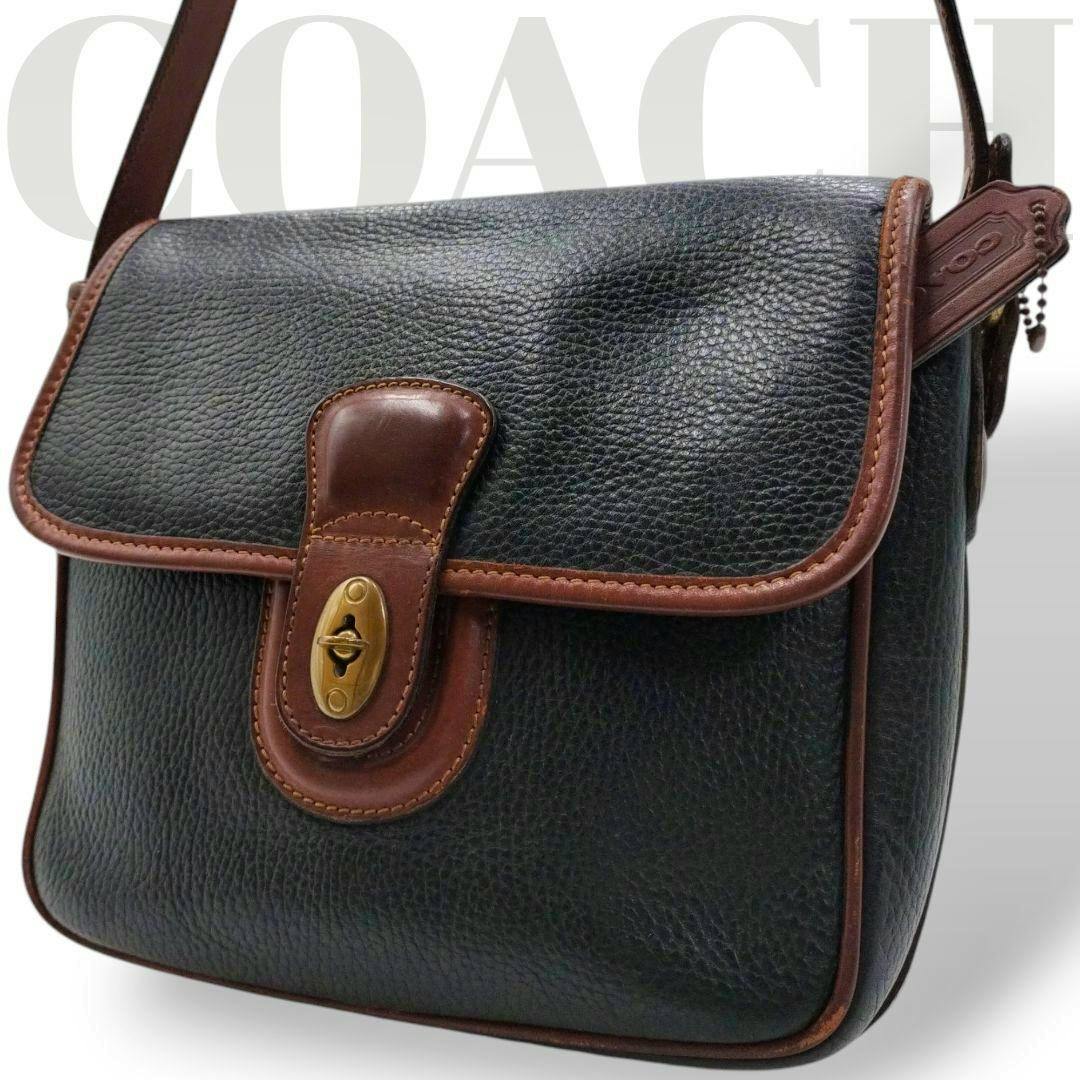 Black pebbled leather Coach shoulder bag with brown leather trim and a brass turn‑lock closure shown in close‑up.