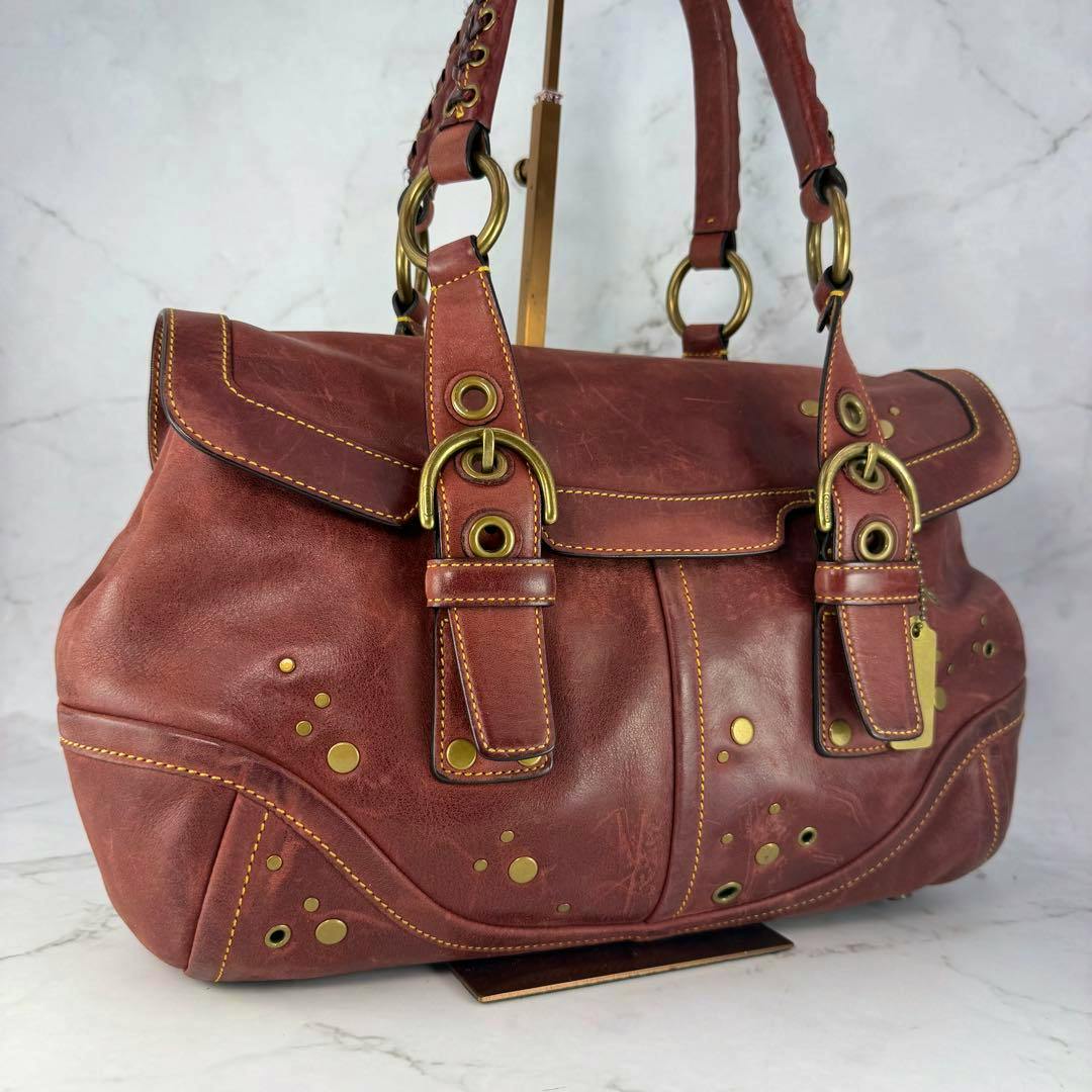 Angled photo of a brown cow leather Coach Soho studded tote bag showing double straps, brass rings, and circular studs.
