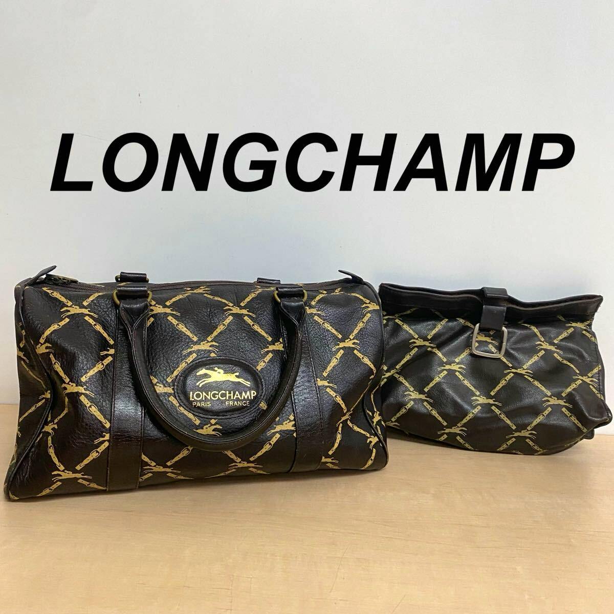 A Longchamp vintage two-piece set showing a Boston bag and matching pouch in dark cow leather with a gold chain pattern, displayed on a table in front of a LONGCHAMP sign.