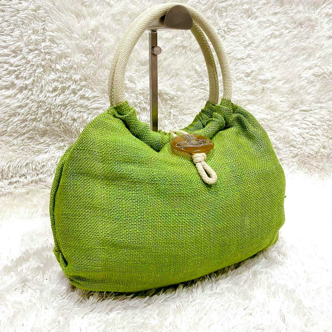Green Vivienne Westwood raffia bag with cream rope handles and an orb button closure on a white fluffy background.