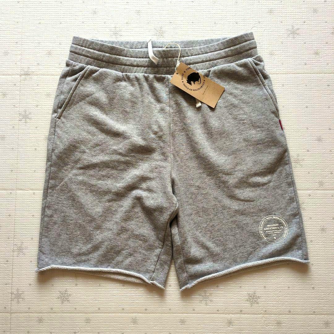 Gray men's cotton sweat shorts laid flat showing the drawstring waistband, side pockets, brand hang tag, and a circular printed logo near the hem.