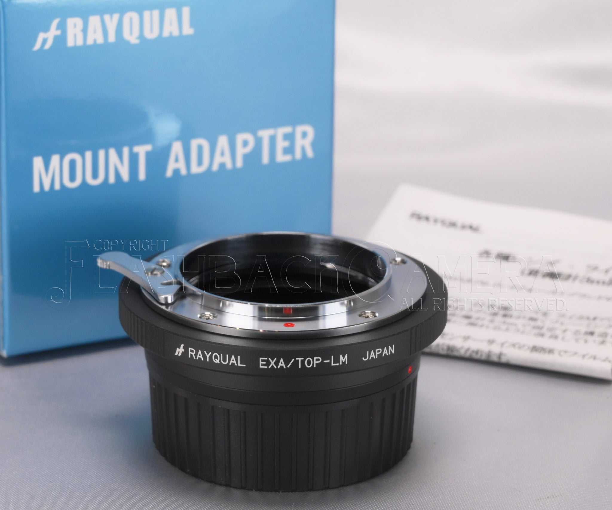 Rayqual EXA-to-LM mount adapter sitting on a surface with its blue Rayqual "Mount Adapter" box and paperwork behind it.
