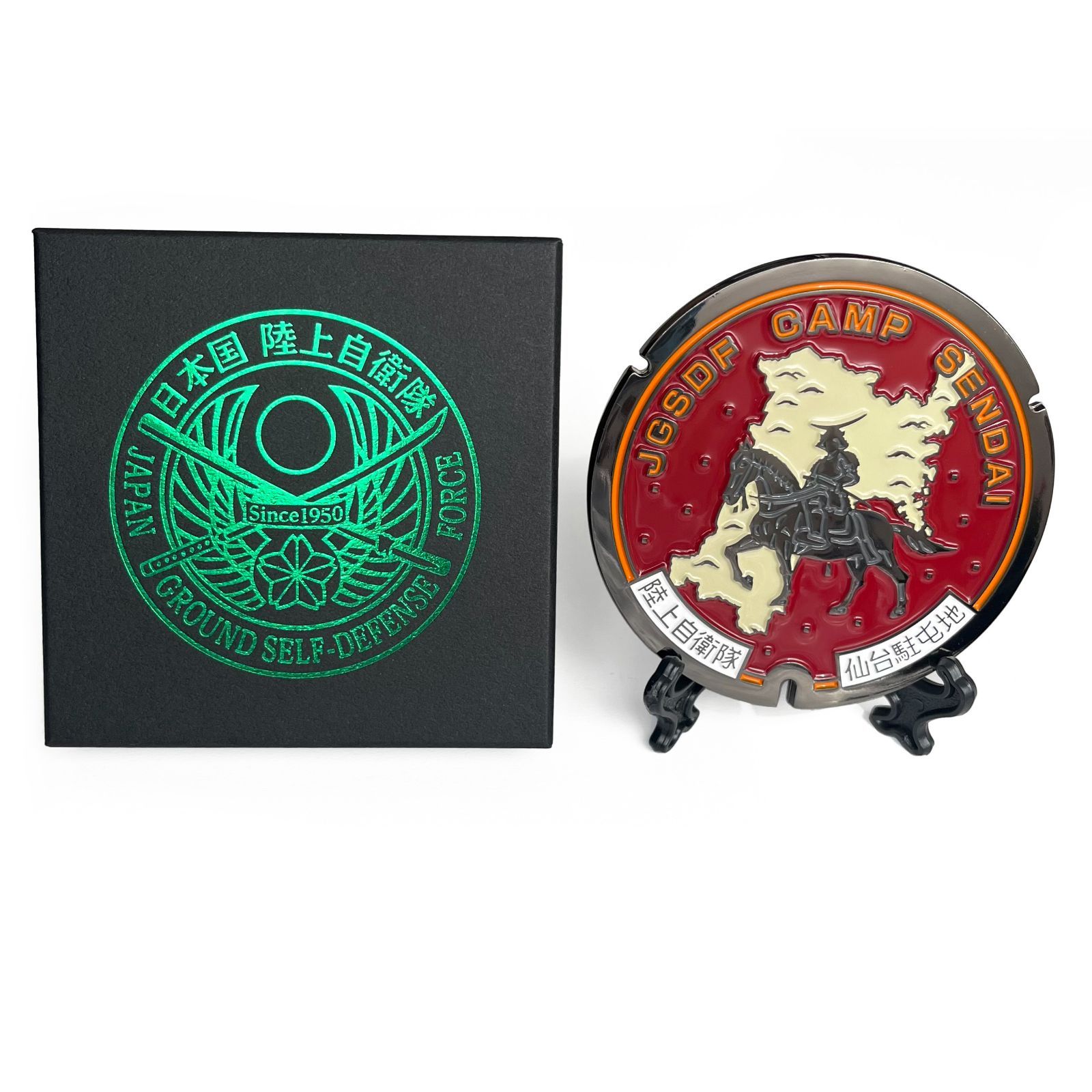 Rubber mini manhole-style coaster with a JGSDF "Camp Sendai" design on a small stand beside its branded box.