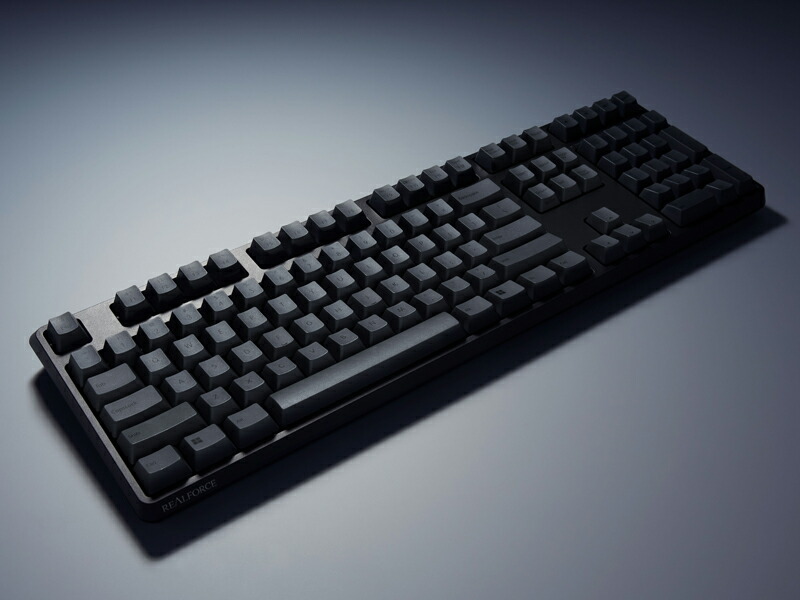 Angled photo of a black and dark-gray REALFORCE R4 English-layout tenkeyless keyboard on a neutral background.
