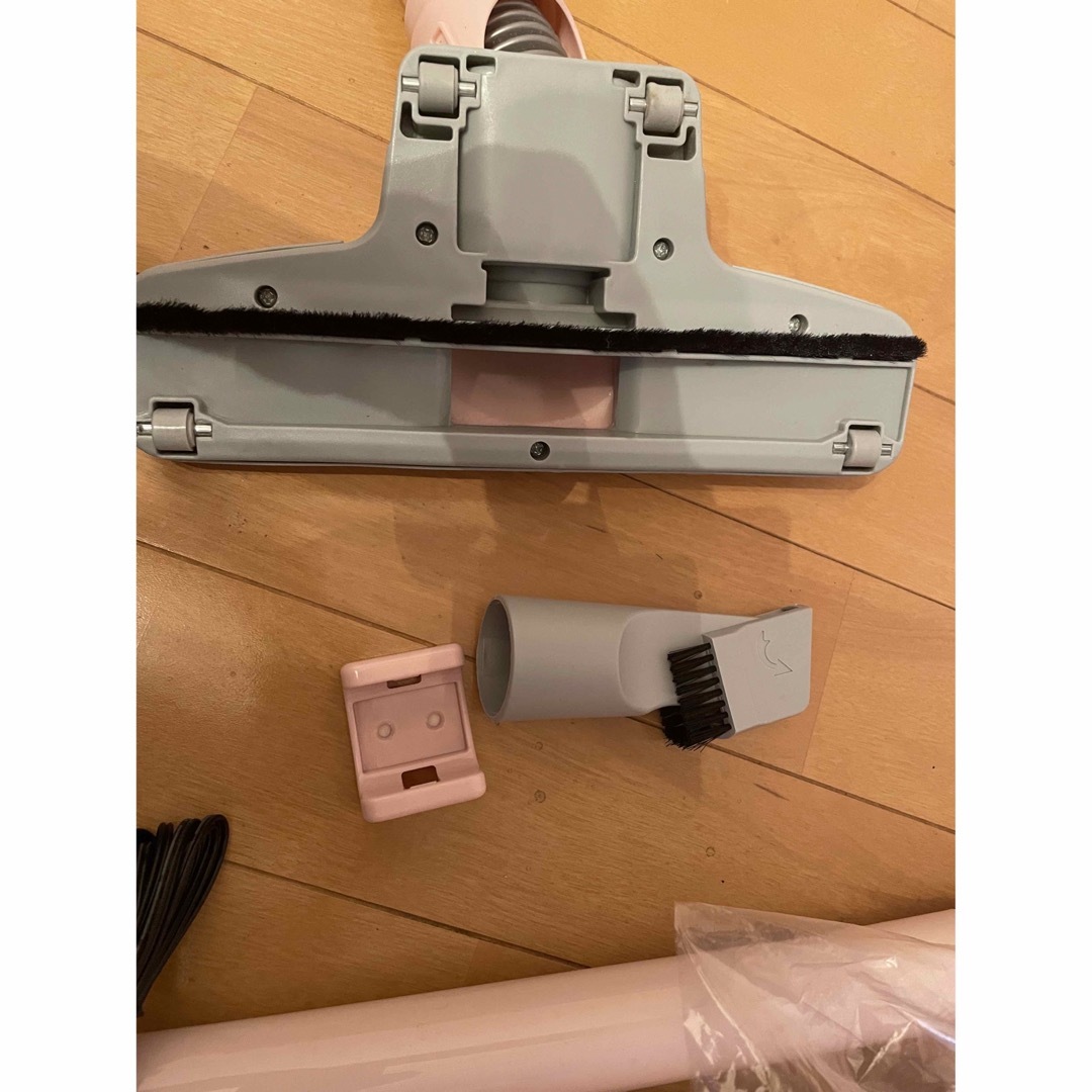 Photo of a cordless vacuum cleaner floor head and two attachments on a wooden floor.