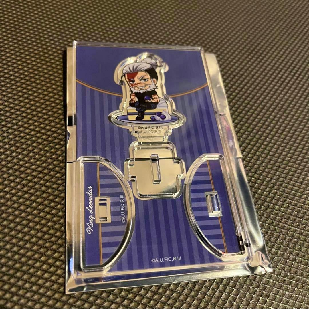 Packaged acrylic decorative stand showing the Leonidas character on a blue striped backing inside a clear plastic sleeve, photographed on a textured surface.