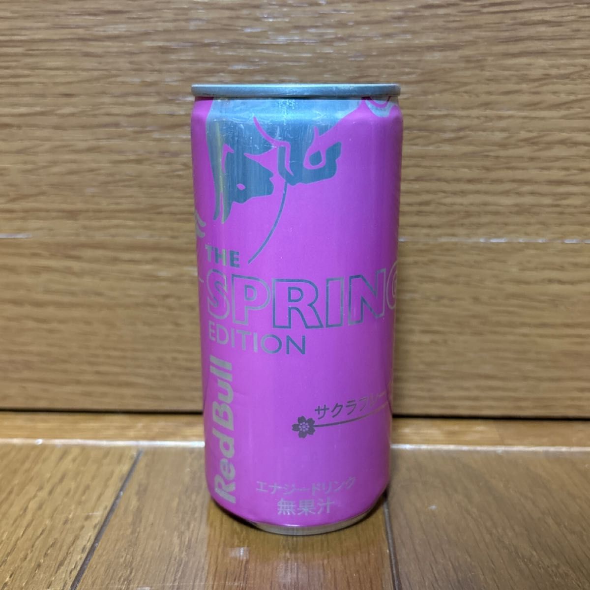 Front view of a pink Red Bull 'The Spring Edition' energy drink can on a wooden surface.