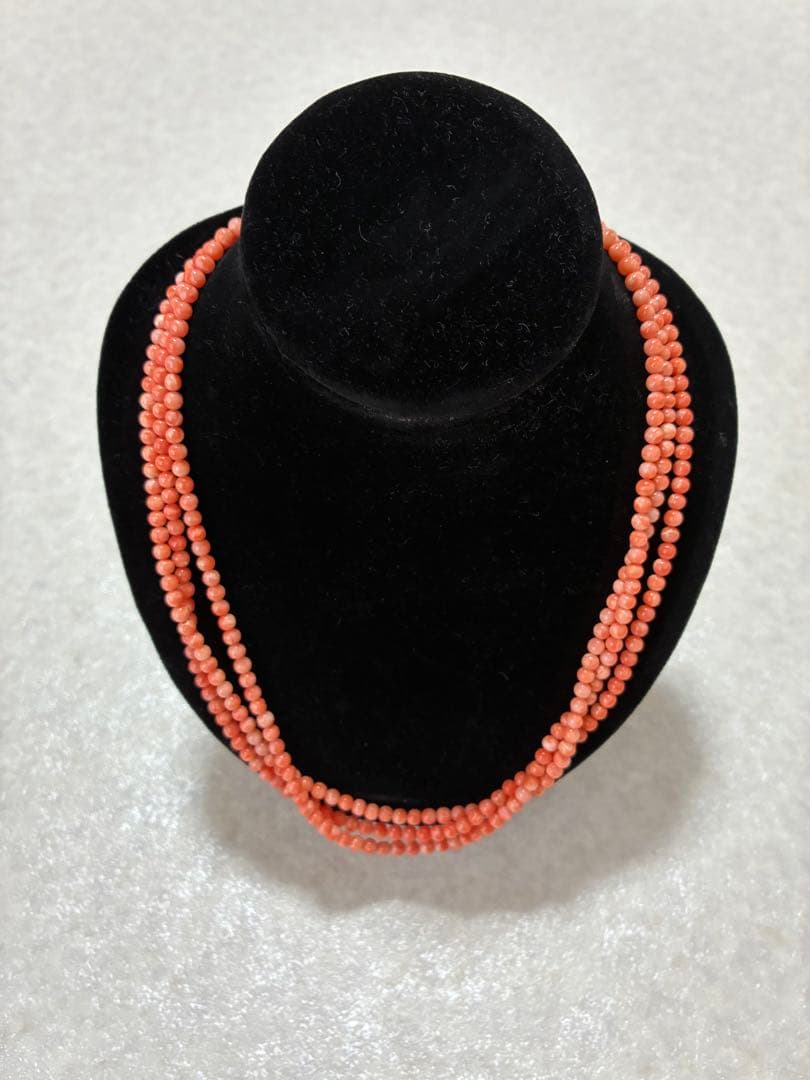 Three-strand red coral bead necklace displayed on a black jewelry bust.