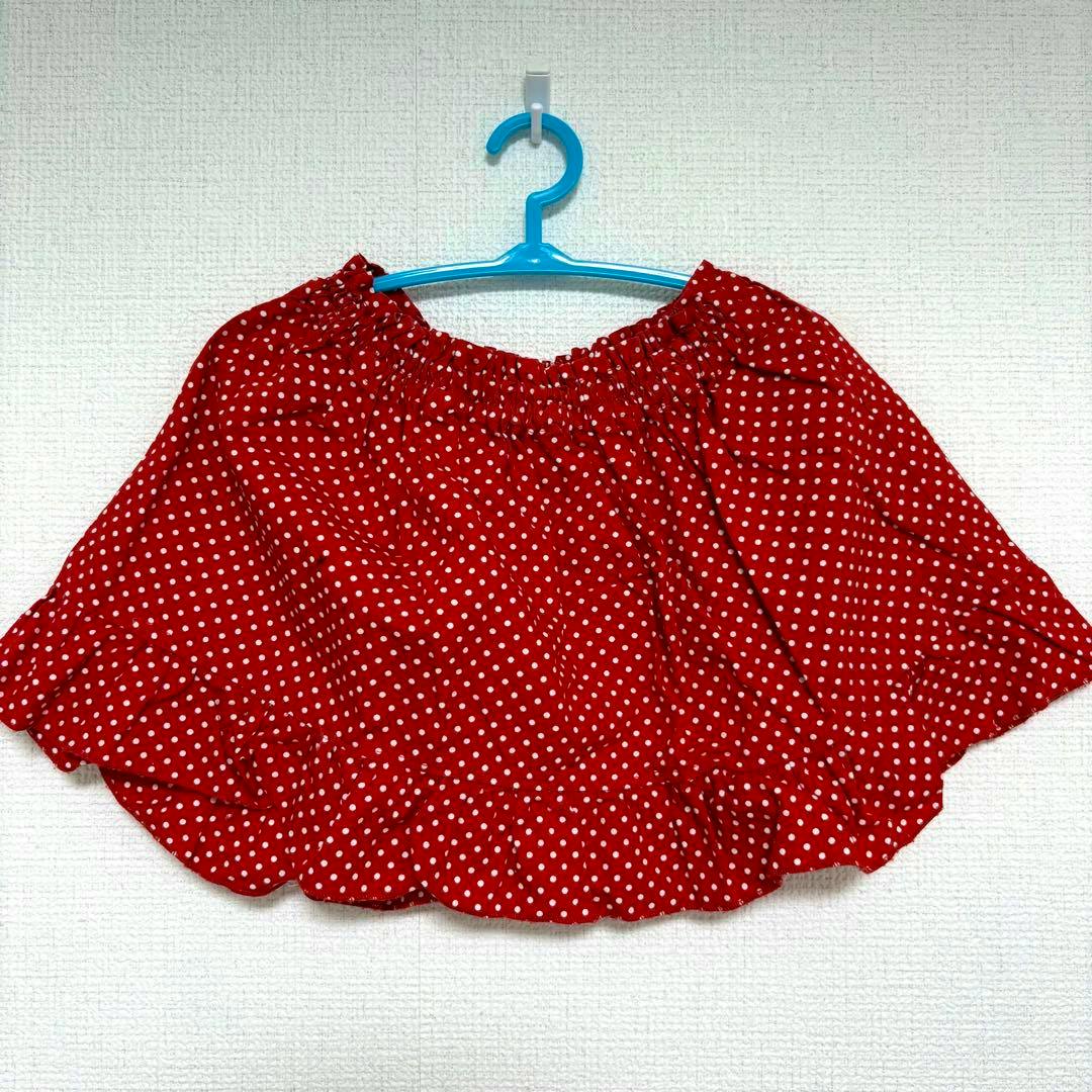 A red polka-dot skirt with a frilled hem hanging on a blue hanger against a white wall.