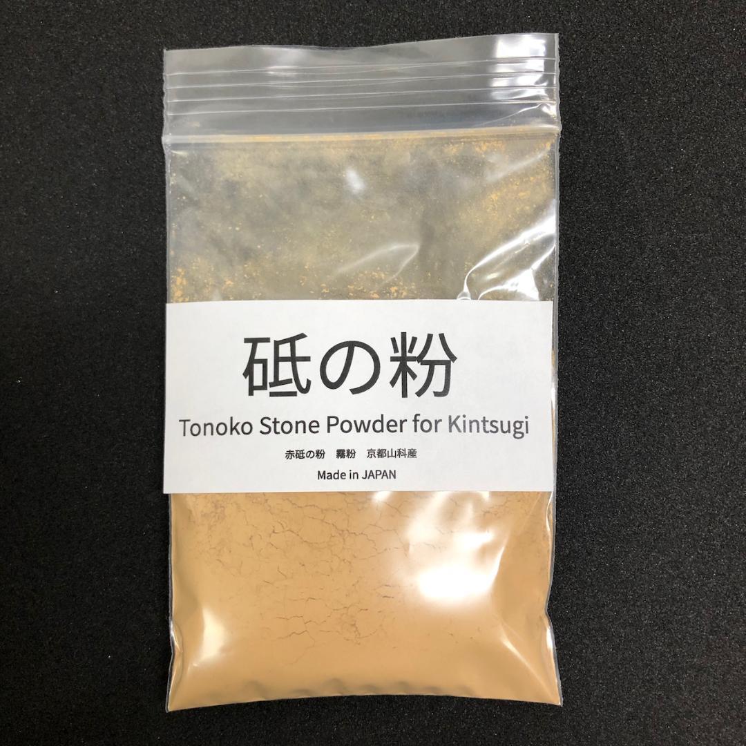 Resealable plastic bag of tan tonoko (stone powder) with a white label reading ‘砥の粉 Tonoko Stone Powder for Kintsugi’ on a black background.