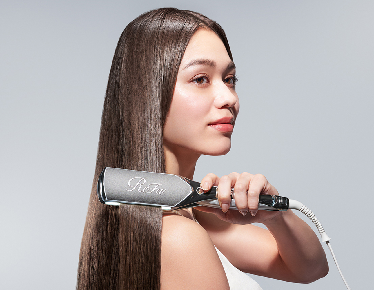 A woman holding and using the ReFa POWER STRAIGHT IRON PRO on long straight hair.