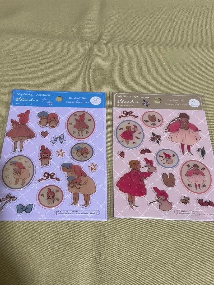 Two packaged Sanrio sticker sheets with pastel character illustrations laid on a fabric background.
