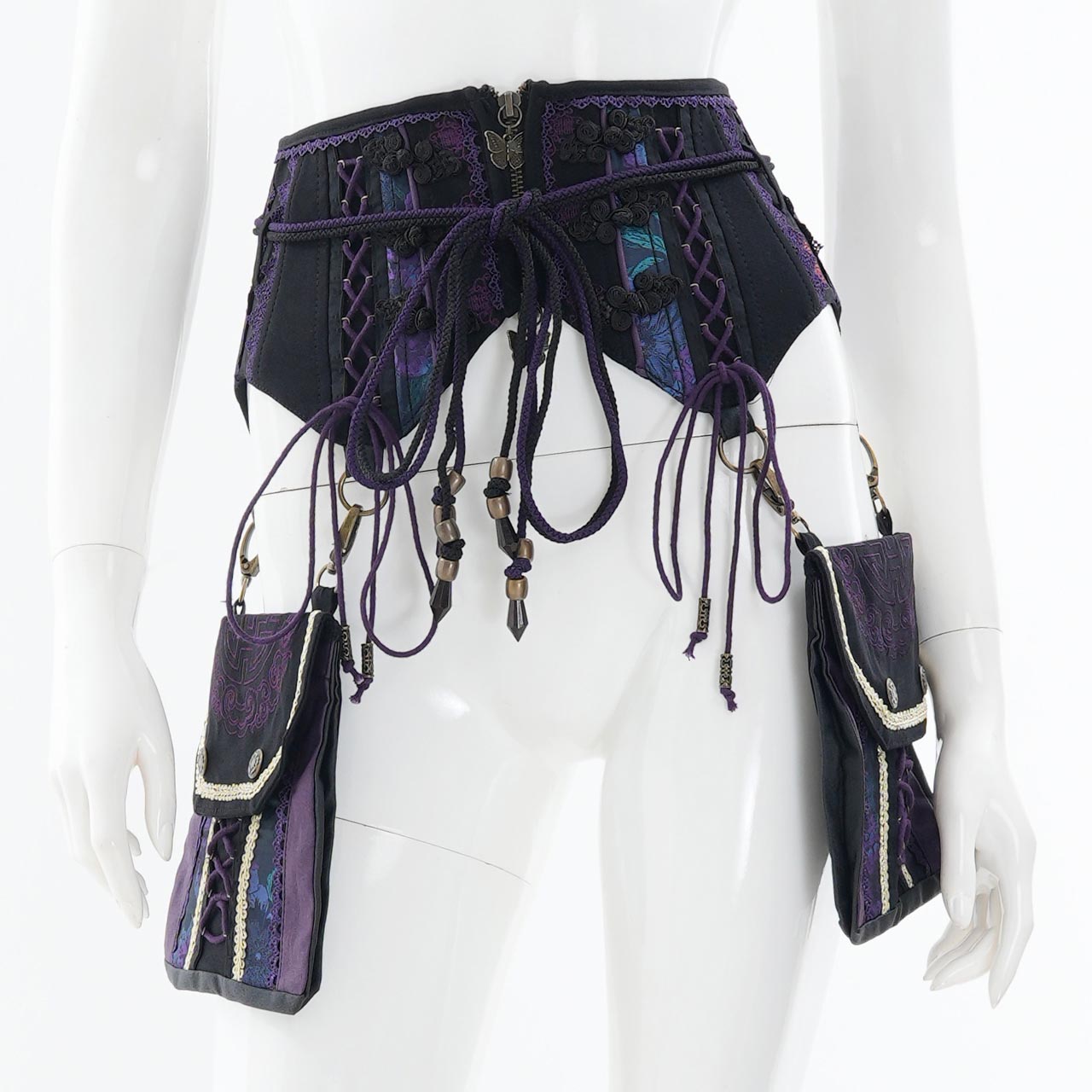 Front view of a purple and black corset with dangling cords and two attached side pouches displayed on a white mannequin.