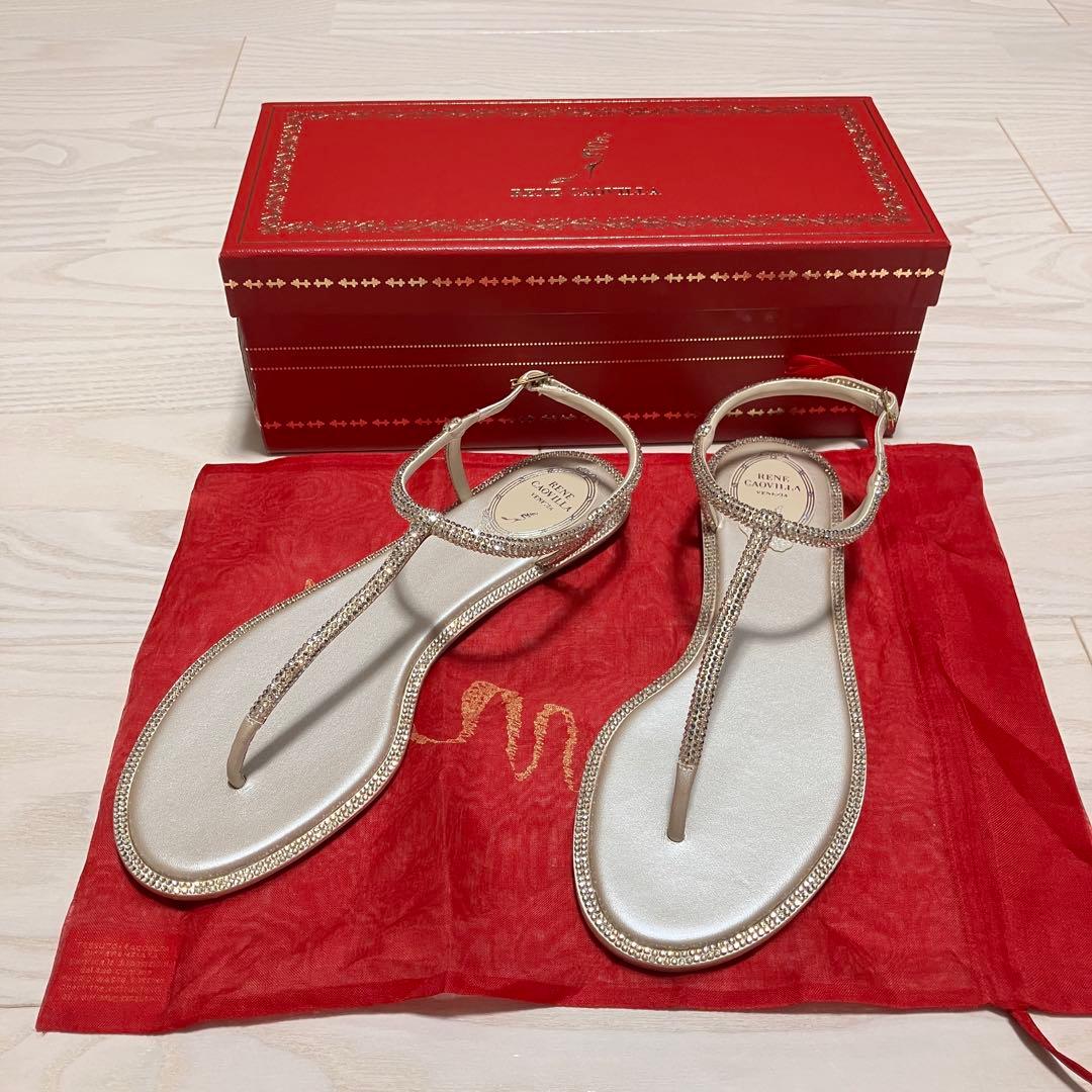 Pair of beige René Caovilla jeweled flat sandals (size 38) displayed with their red box and red dust bag on a light wood floor.