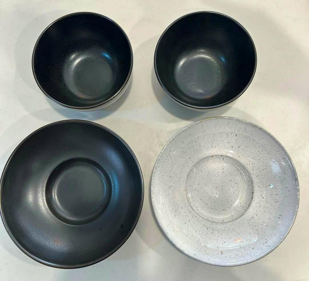 Top-down photo of the four-piece RENE OZORIO WABI SABI MIYAMA set showing two black bowls and two shallow plates (one black, one white-speckled).