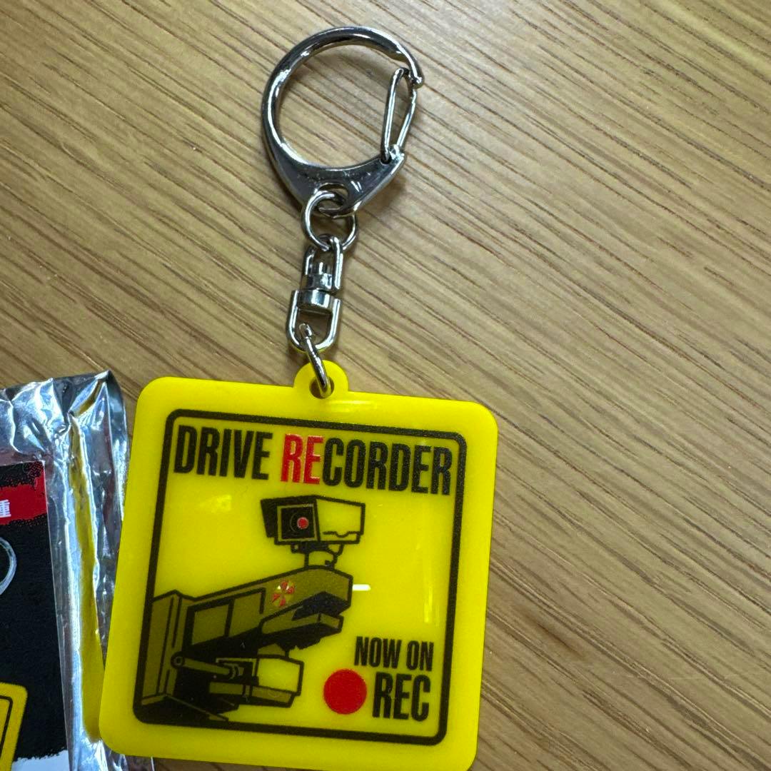 Yellow acrylic keychain with metal clasp showing a camera graphic and the text "DRIVE RECORDER" and "NOW ON REC".