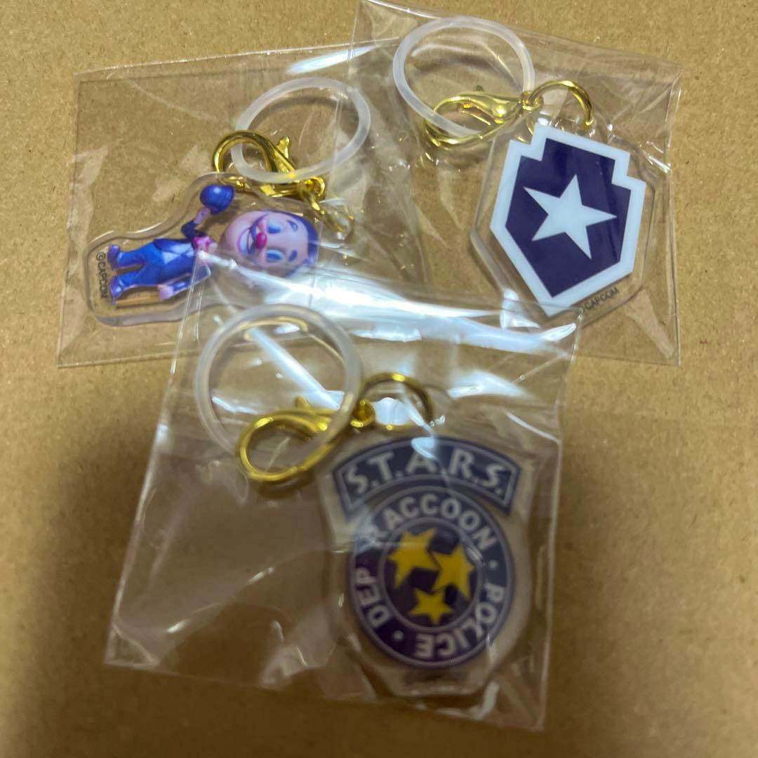 Three sealed acrylic keychain umbrella markers with Resident Evil–themed designs (S.T.A.R.S. badge, star shield, and a character) on a cardboard background.