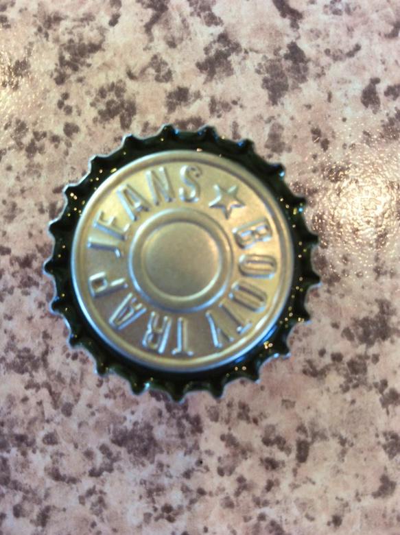A resin fridge magnet shaped like a bottle cap with raised lettering and a dark scalloped edge on a speckled surface.
