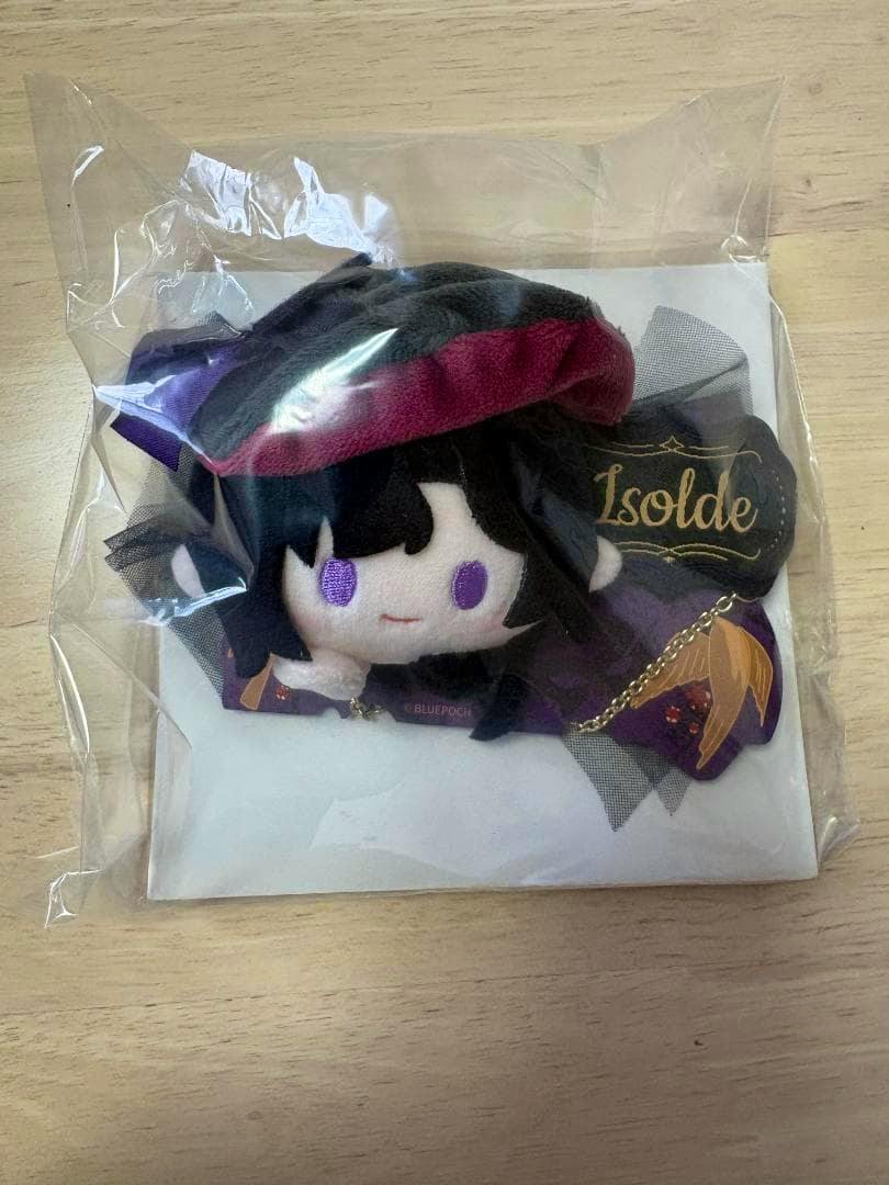 Isolde plush can badge in clear plastic packaging placed on a wooden surface.
