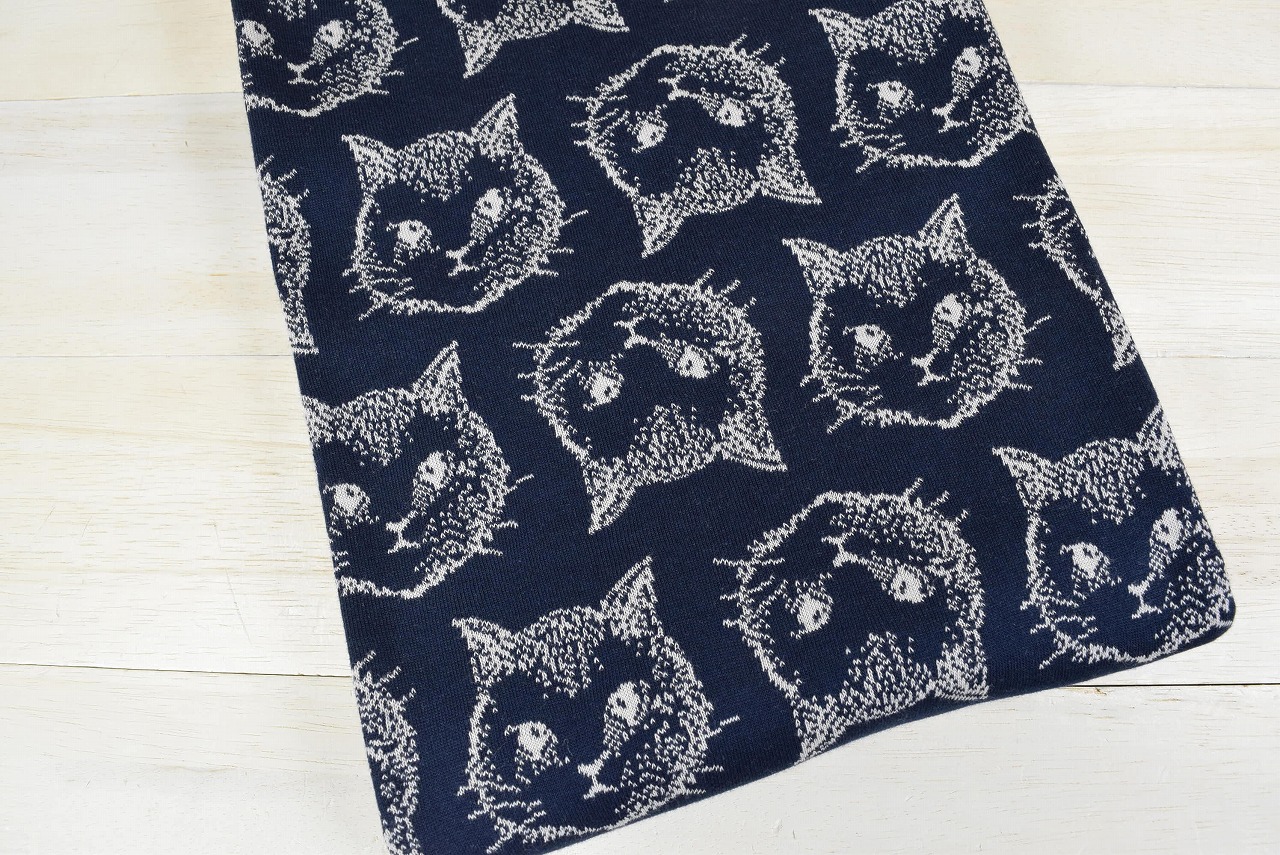 Navy jacquard knit fabric with a repeating cat-head (シャトン柄) pattern laid flat on a light wood surface.