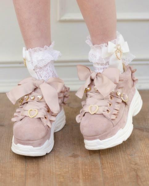 Pair of pink thick-soled sneakers with jeweled belt straps and large ribbon bows worn with lace socks.