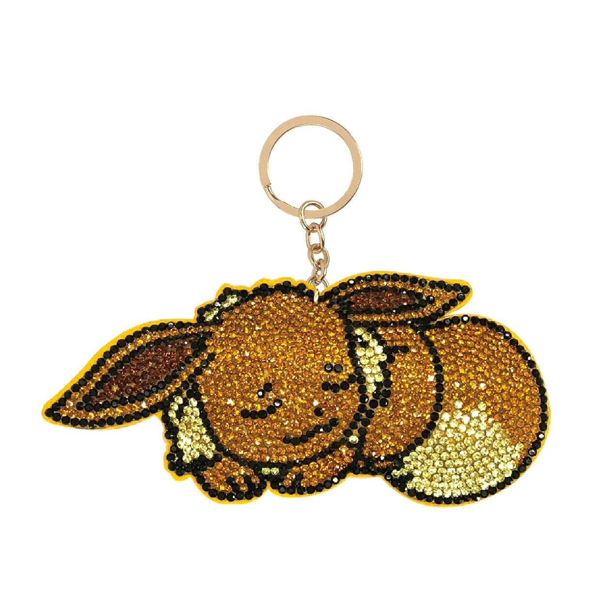 Close-up photo of a rhinestone Eevee mascot keychain cleaner with a gold key ring on a white background.