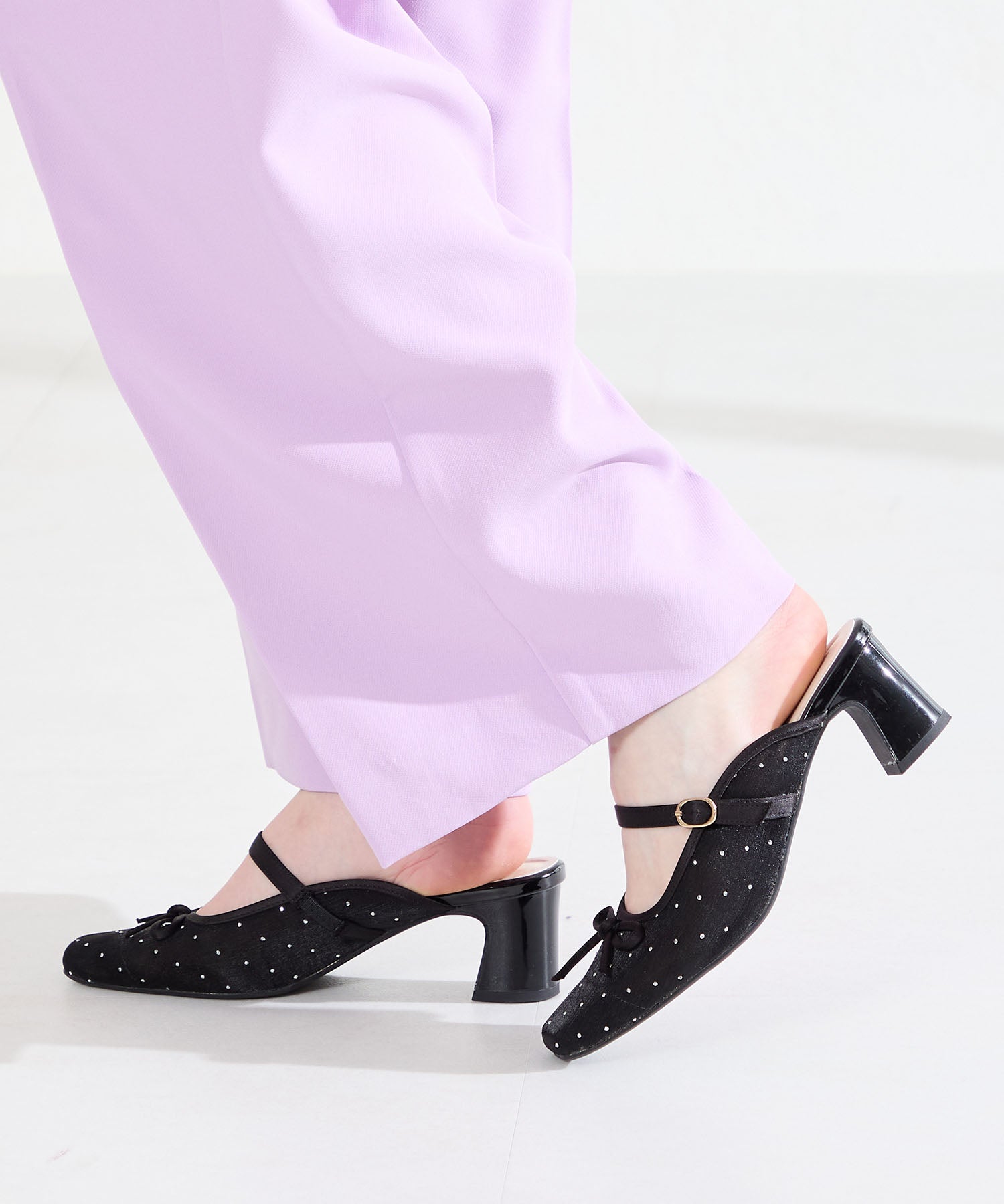 Black rhinestone-and-ribbon sheer pumps with a mid block heel shown on a model's feet.