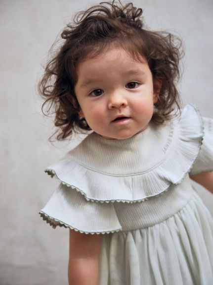 A baby wearing the rib scallop frill organic cotton bib.