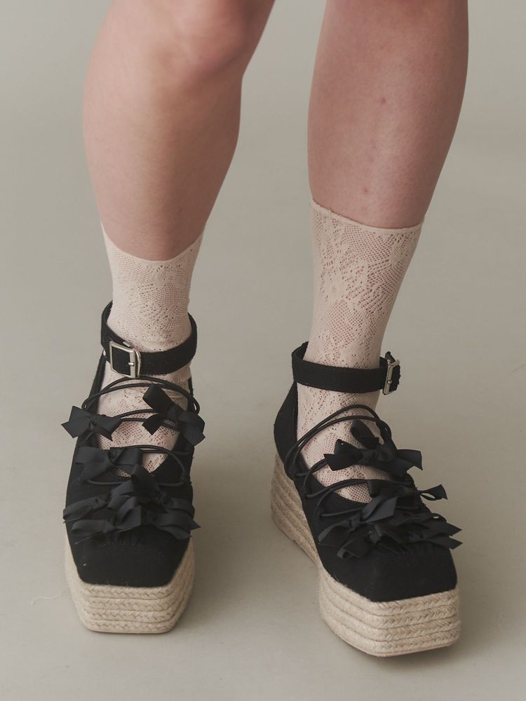 Black ribbon ballet jute wedge sandals worn on a model's feet showing ankle straps, ribbon lacing, and the jute platform.