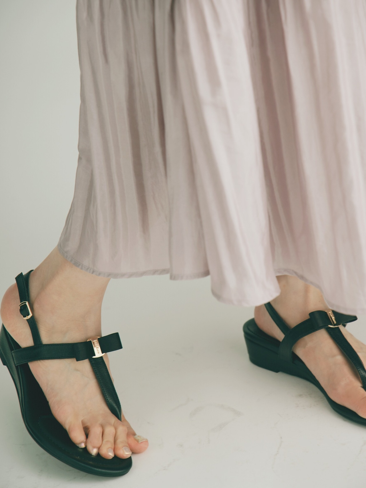 Close-up of a model's feet wearing ribbon flat rubber sandals with ankle straps and buckles.