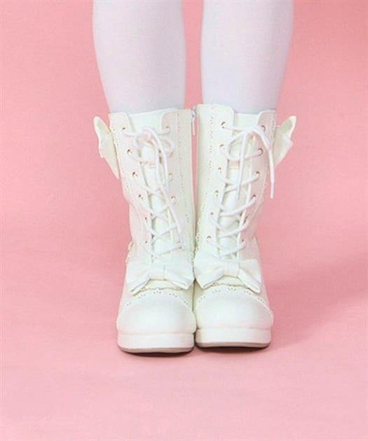 Front view of white ribbon mid-height synthetic leather boots worn on a model's legs against a pink background.