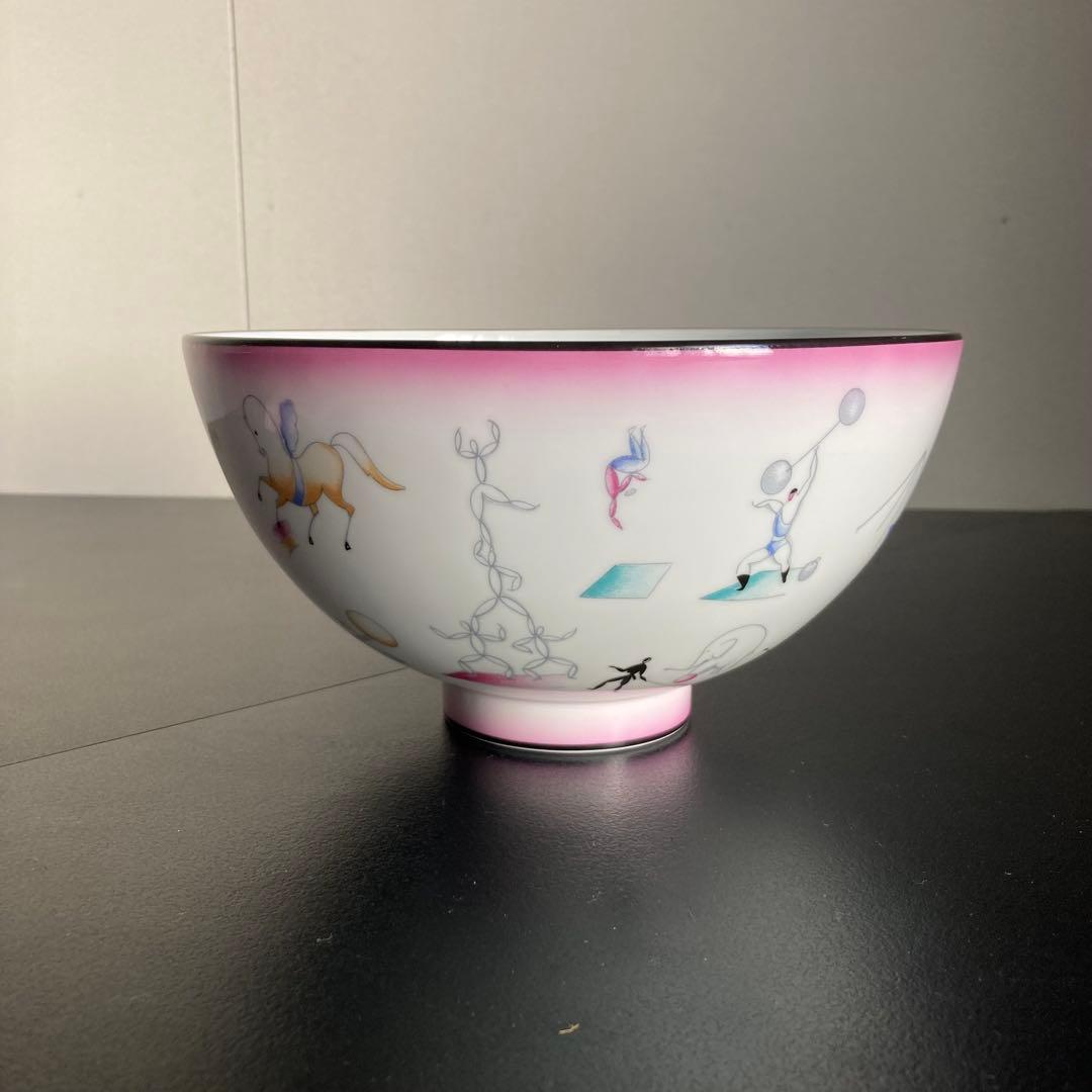 Porcelain bowl showing circus-themed illustrations and a pink rim, side view.
