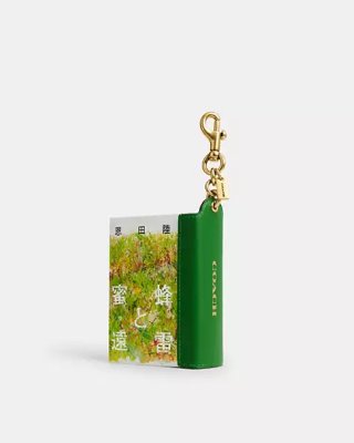 Green leather book-shaped bag charm keychain with a gold clasp and a miniature cover of 恩田陸『蜜蜂と遠雷』.