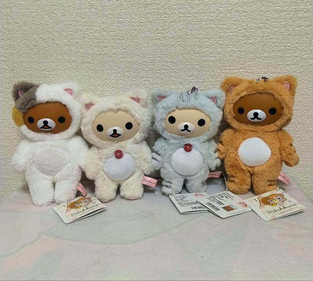 Four Rilakkuma plush figures in cat costumes arranged side by side, showing the full set of four toys.