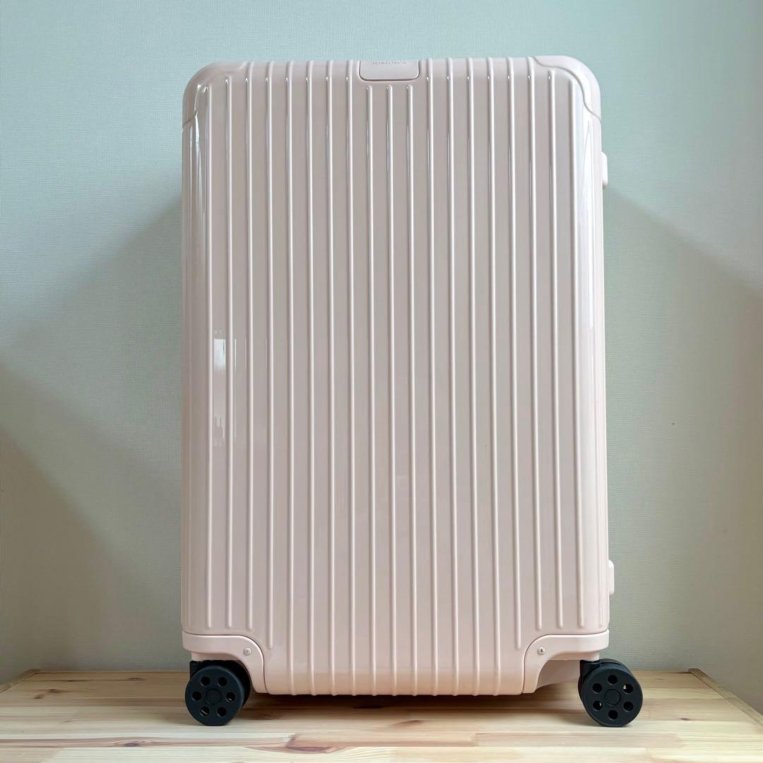 Front view of a pale pink RIMOWA Essential Check-In L hard-shell suitcase standing upright on a wooden surface.