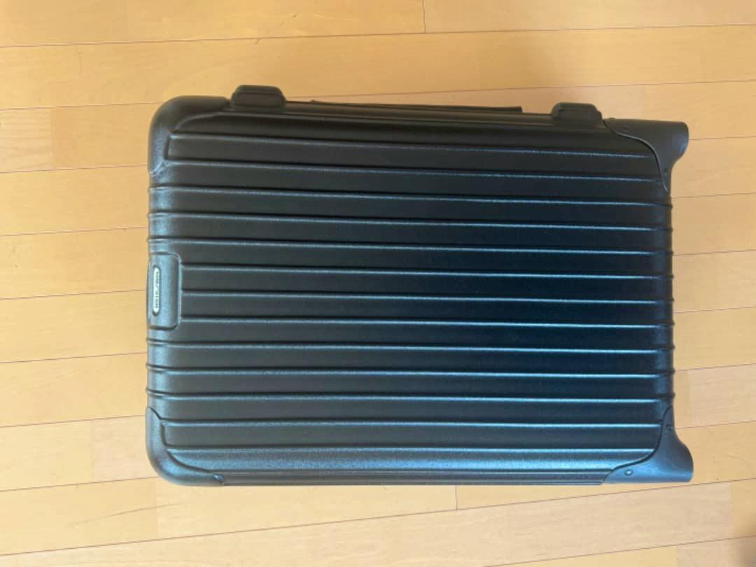 Top-down view of a black RIMOWA Salsa 35L carry-on hard-shell suitcase lying on a wooden floor.