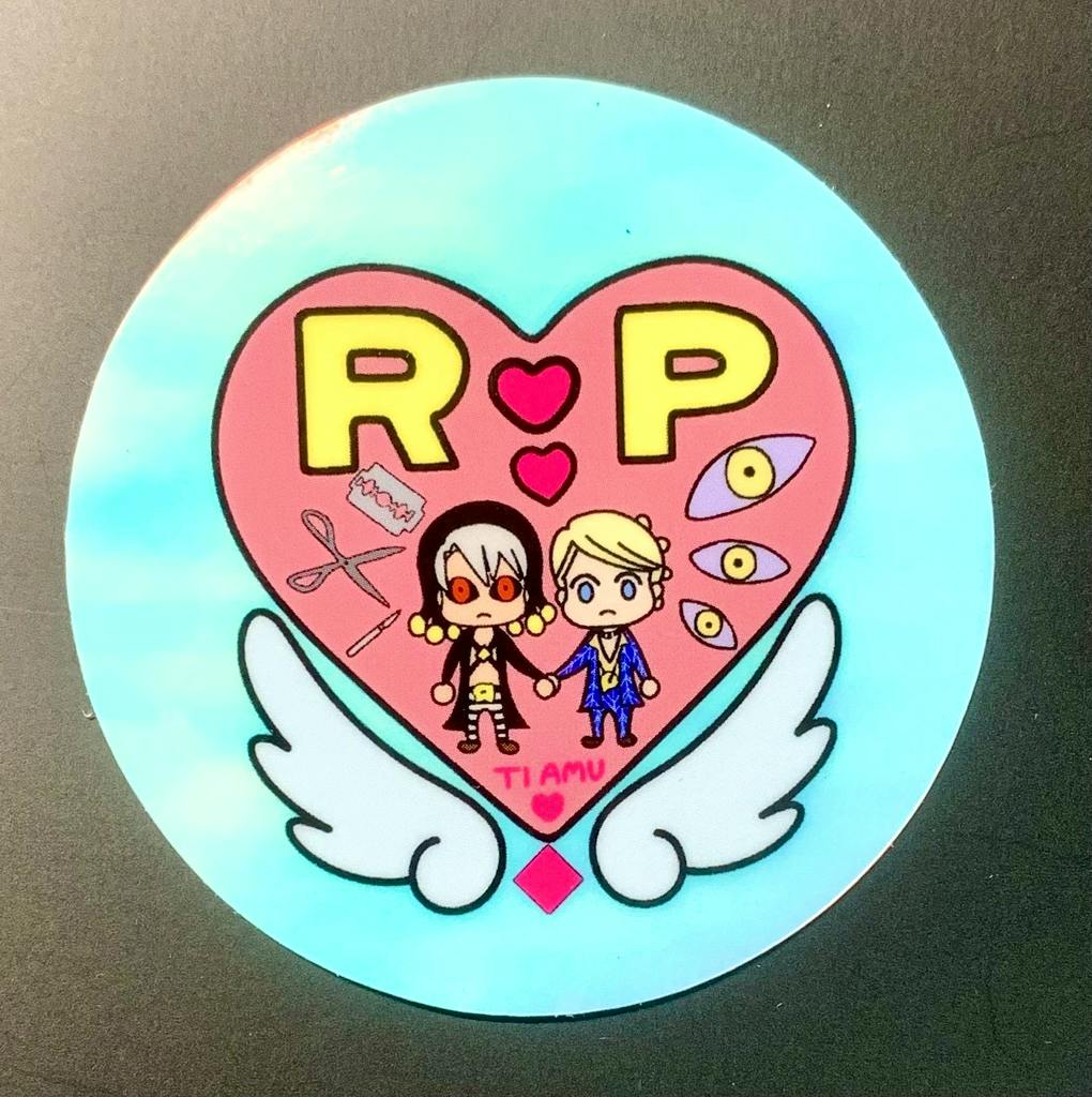 Round paper sticker showing a pink heart with two small cartoon characters, yellow "R P" letters, and white wings on a blue circular background.