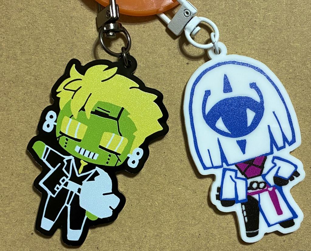 Two acrylic character keychains, one green and one white, lying on a brown surface with their metal clasps visible.