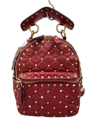 Red quilted backpack with gold studs, front zip pocket, top handle, and visible zipper hardware.