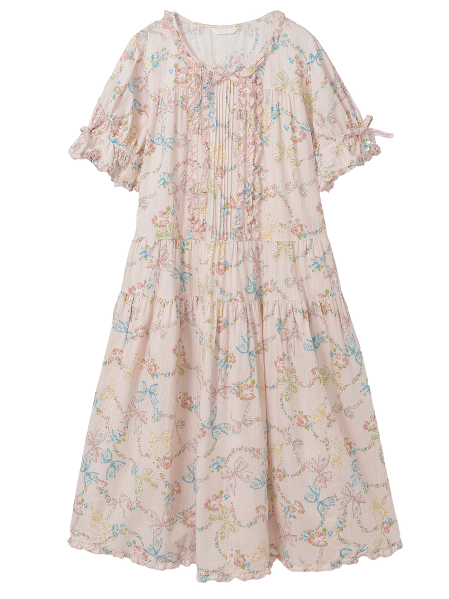 Front view of a pink midi cotton dress with rococo ribbon and floral print, short ruffled sleeves, and a tiered skirt.