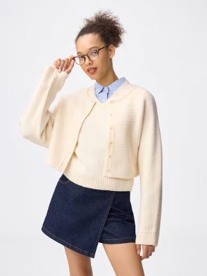 Model wearing the 2-piece knit mini dress by rokh in cream, shown with a collared shirt and denim skirt.