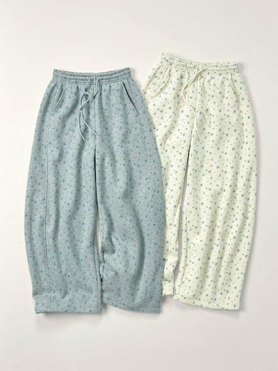 Two floral-print sweatpants, one light blue and one cream, laid flat on a neutral background.