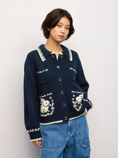 Model wearing a navy polo-style cardigan with contrasting white trim, decorative pocket motifs, and large front buttons.