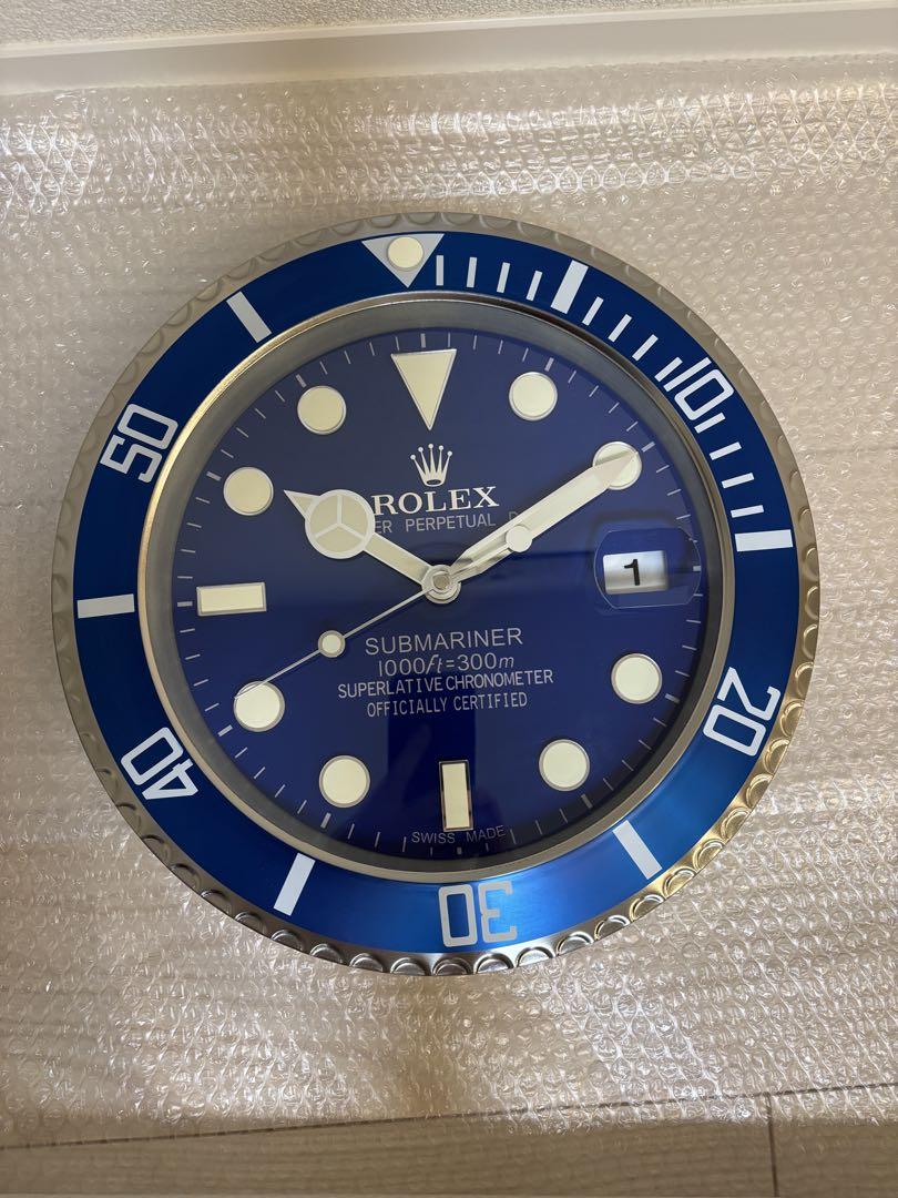 Front view of the wall clock showing a blue Rolex Submariner-style dial with hands and a date magnifier at 3 o'clock.