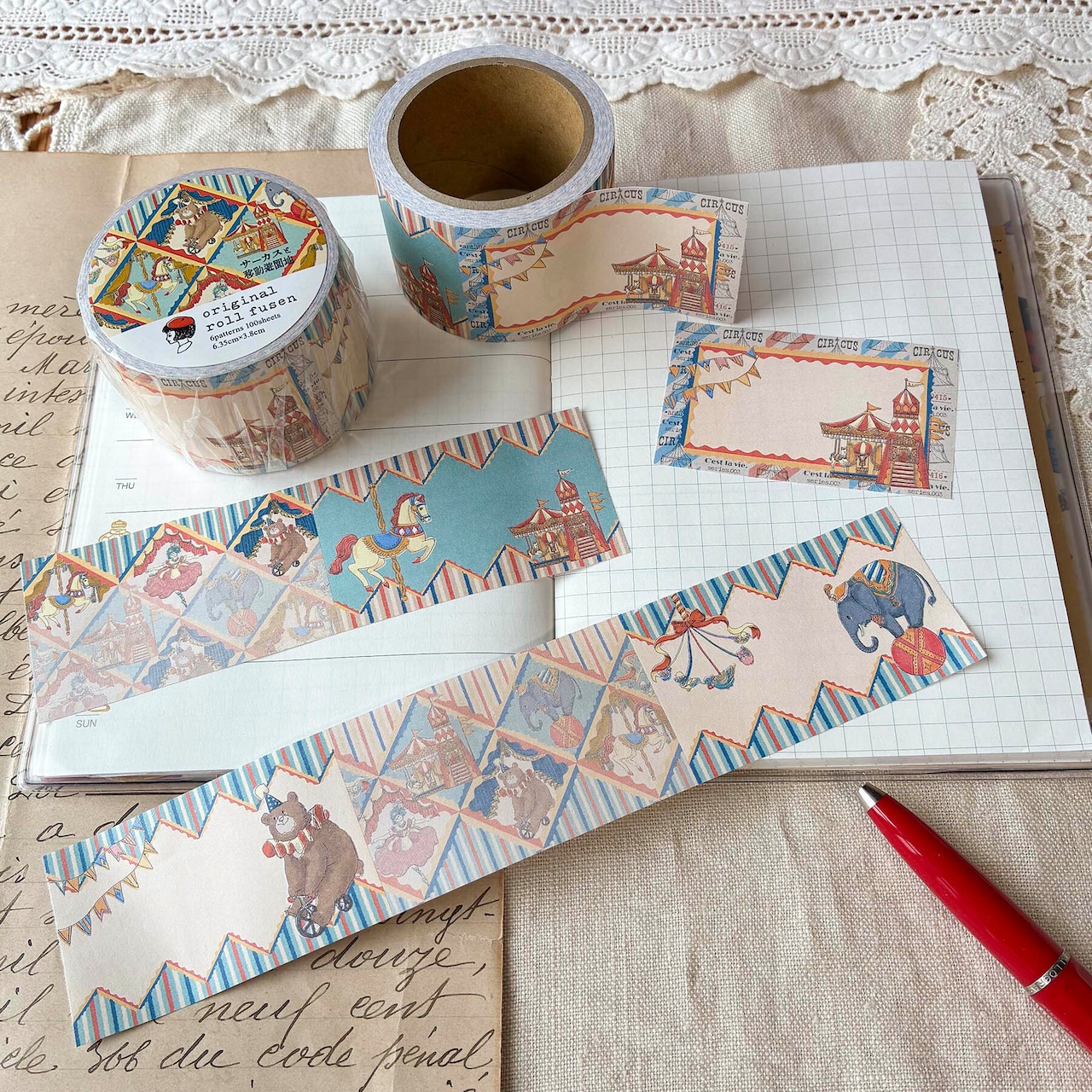 A roll-type sticky note set with circus and amusement-park illustrations, showing two rolls and several torn strips arranged on an open notebook.