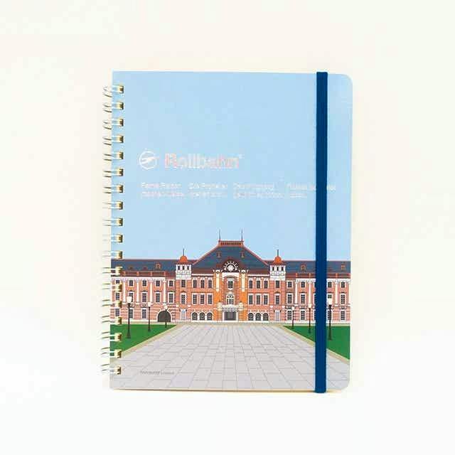 Rollbahn L pocket notebook with Tokyo Station (Marunouchi Central Plaza) illustration on a light blue cover, gold spiral binding and dark blue elastic band.