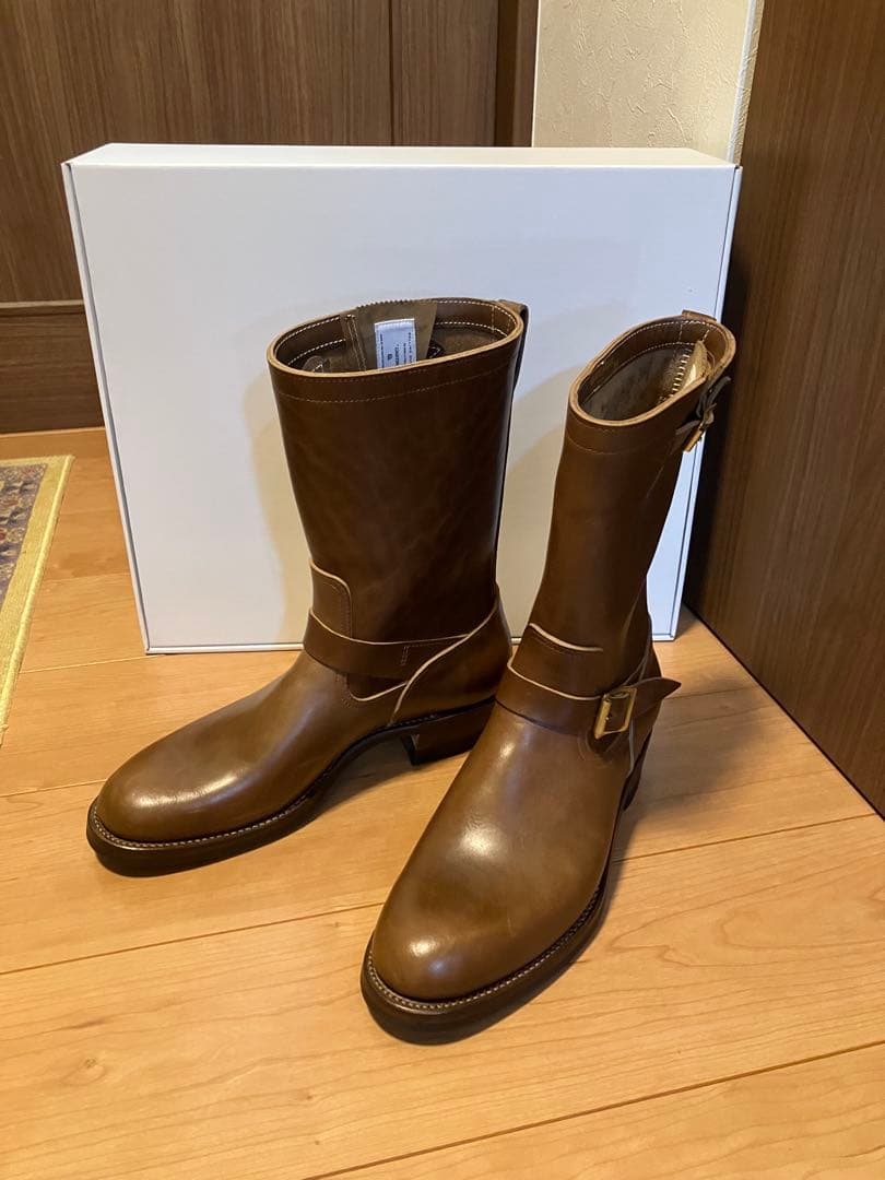 Pair of brown leather engineer boots standing on a wooden floor in front of a white box.