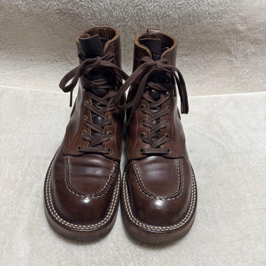 Pair of brown leather moc-toe boots shown from the front on a light fabric background.